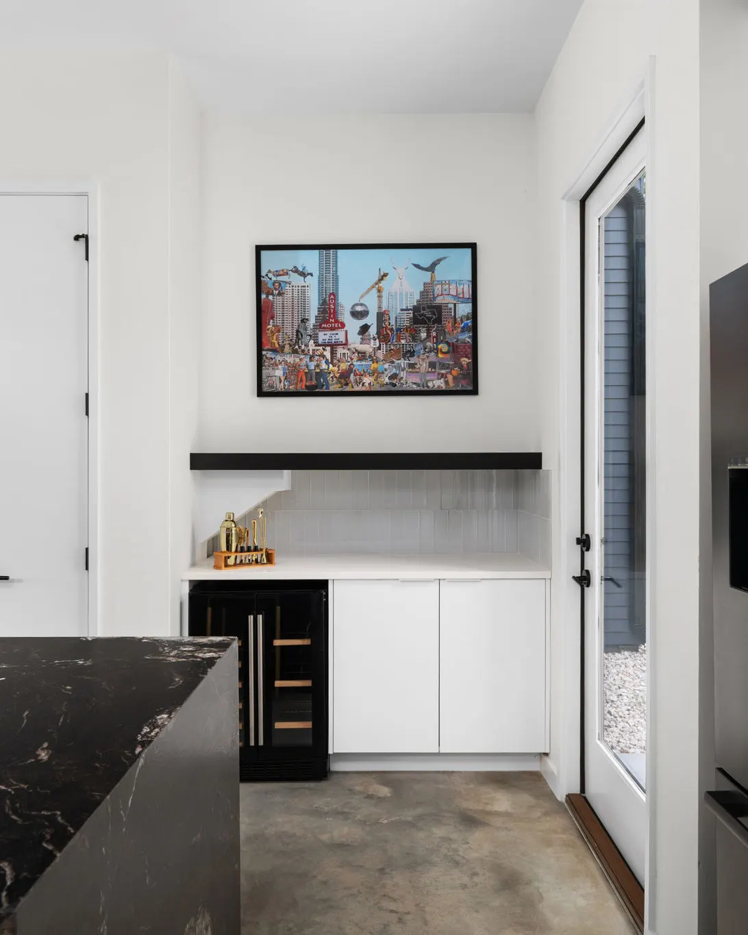 A bar nook with a wine fridge, a gold cocktail set and a colorful Austin collage print above the counter