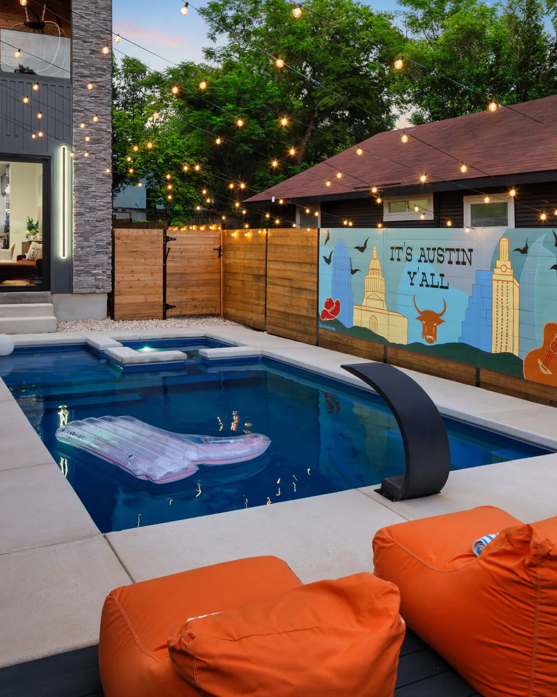 The pool at dusk under string lights, with a mural by a local artist on the fence reading "It's Austin Y'all" and showing the Capitol, the UT Tower and a longhorn
