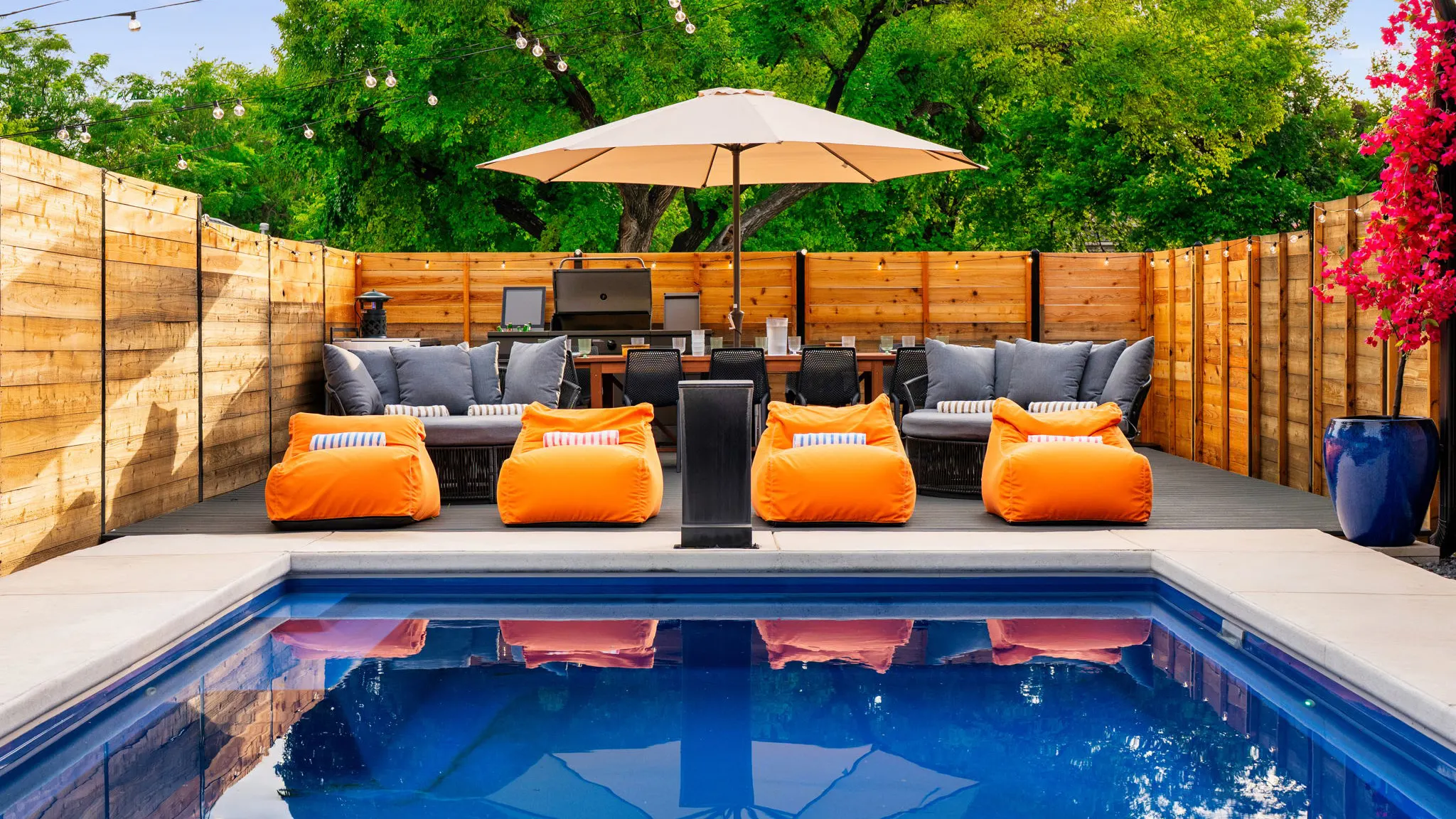 The pool with four orange loungers at its edge, outdoor sofas and a dining table under an umbrella behind them