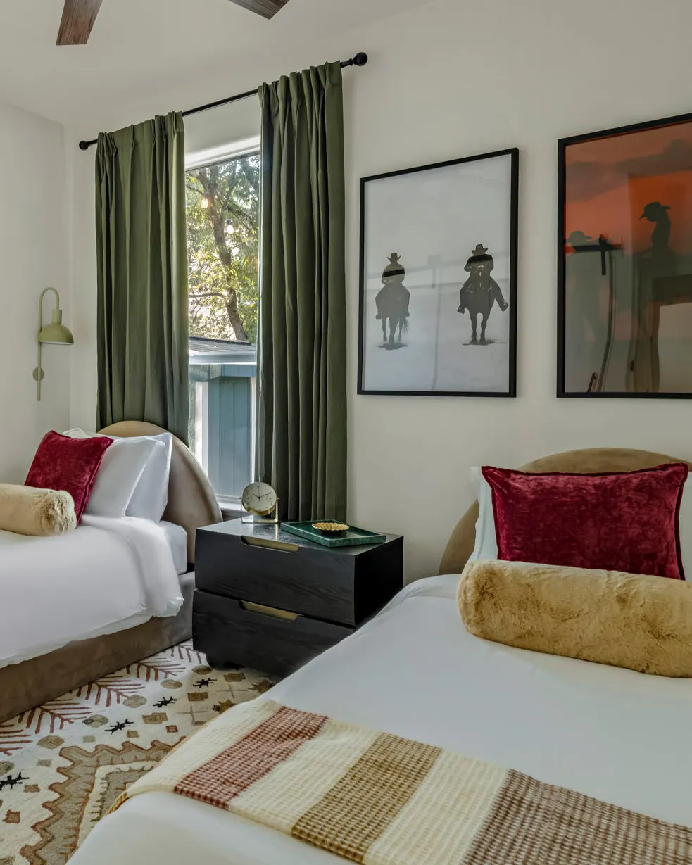 Two beds with red velvet pillows and faux fur bolsters beneath framed photographs of cowboys on horseback