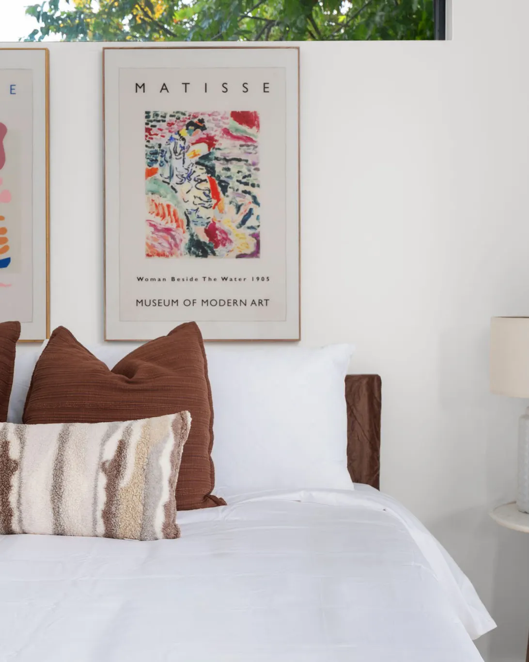 A bed with brown and shaggy striped pillows beneath framed Matisse exhibition posters