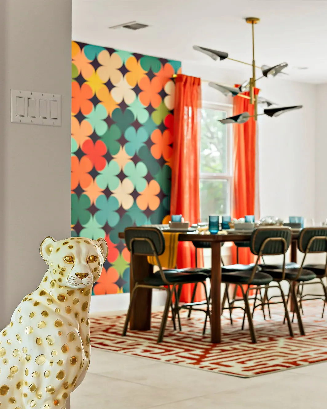 A ceramic leopard statue in the foreground, with the dining table beyond against a bold patterned feature wall and orange curtains