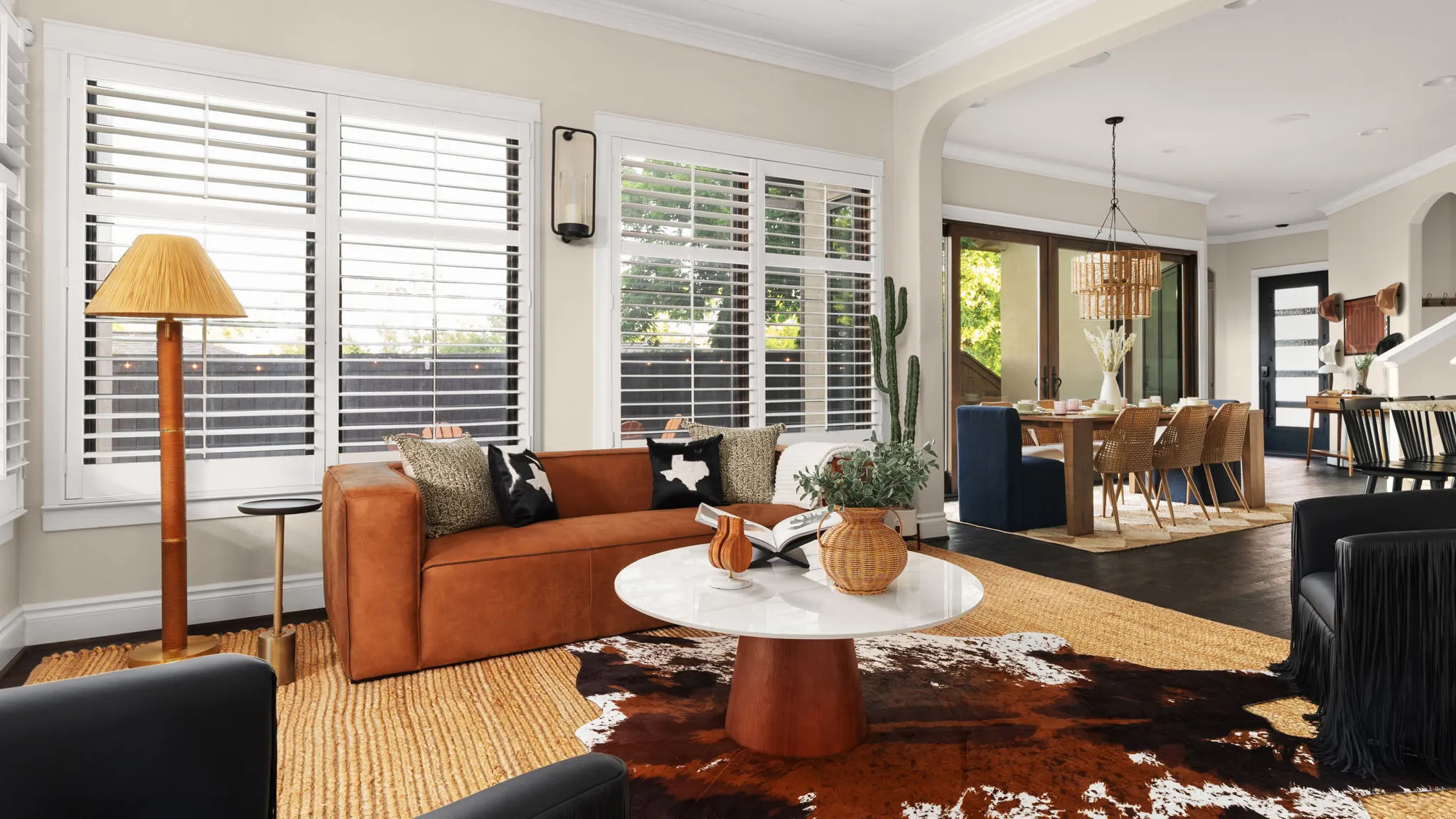 The living room after the redesign: a cognac leather sofa, a round white coffee table on a cowhide rug, and the dining area beyond