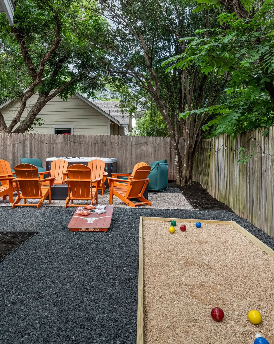 A bocce court with scattered balls in the foreground, and a Longhorns cornhole board and orange Adirondack chairs around the hot tub beyond