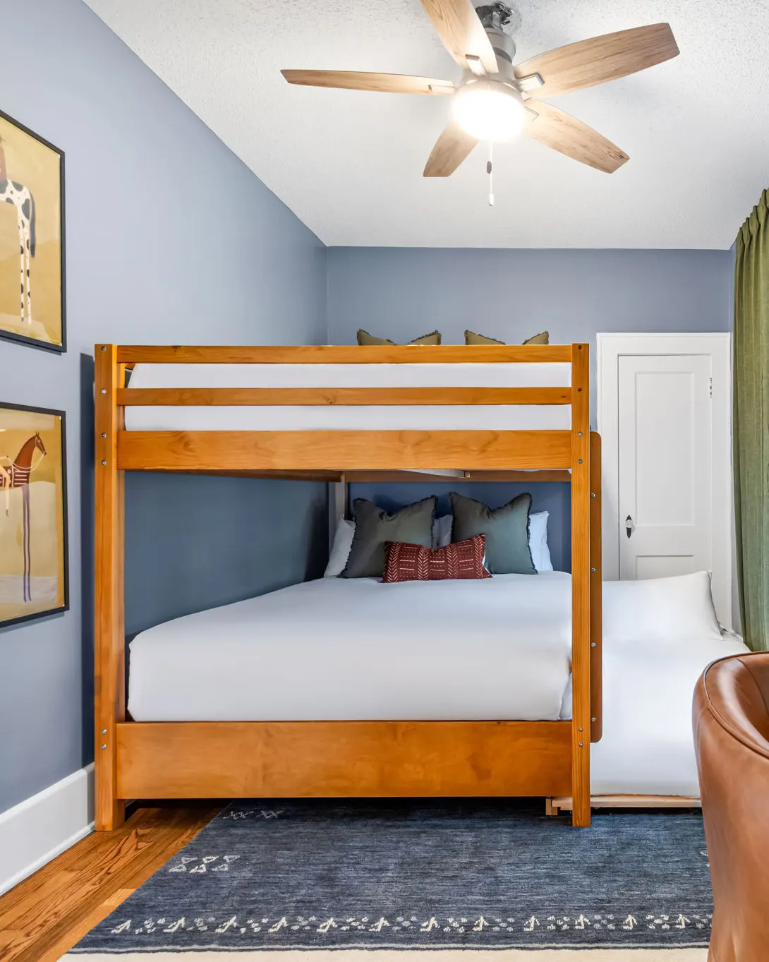 A bunk room with a wooden bunk bed and a wide lower bunk, blue walls and two horse prints