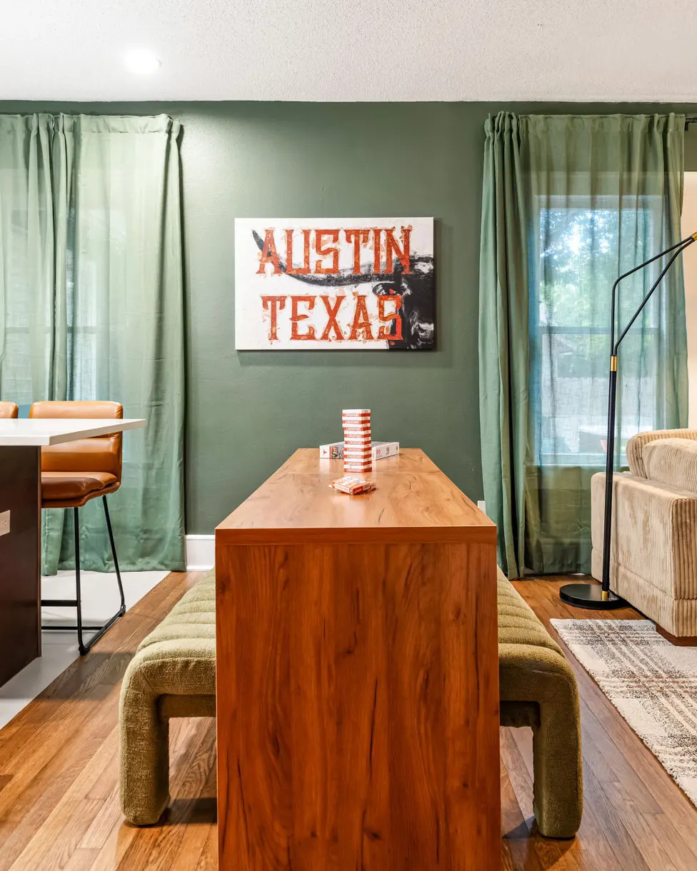 A wooden high table with green upholstered benches and a block-stacking game, beneath an "Austin Texas" longhorn sign on a green wall