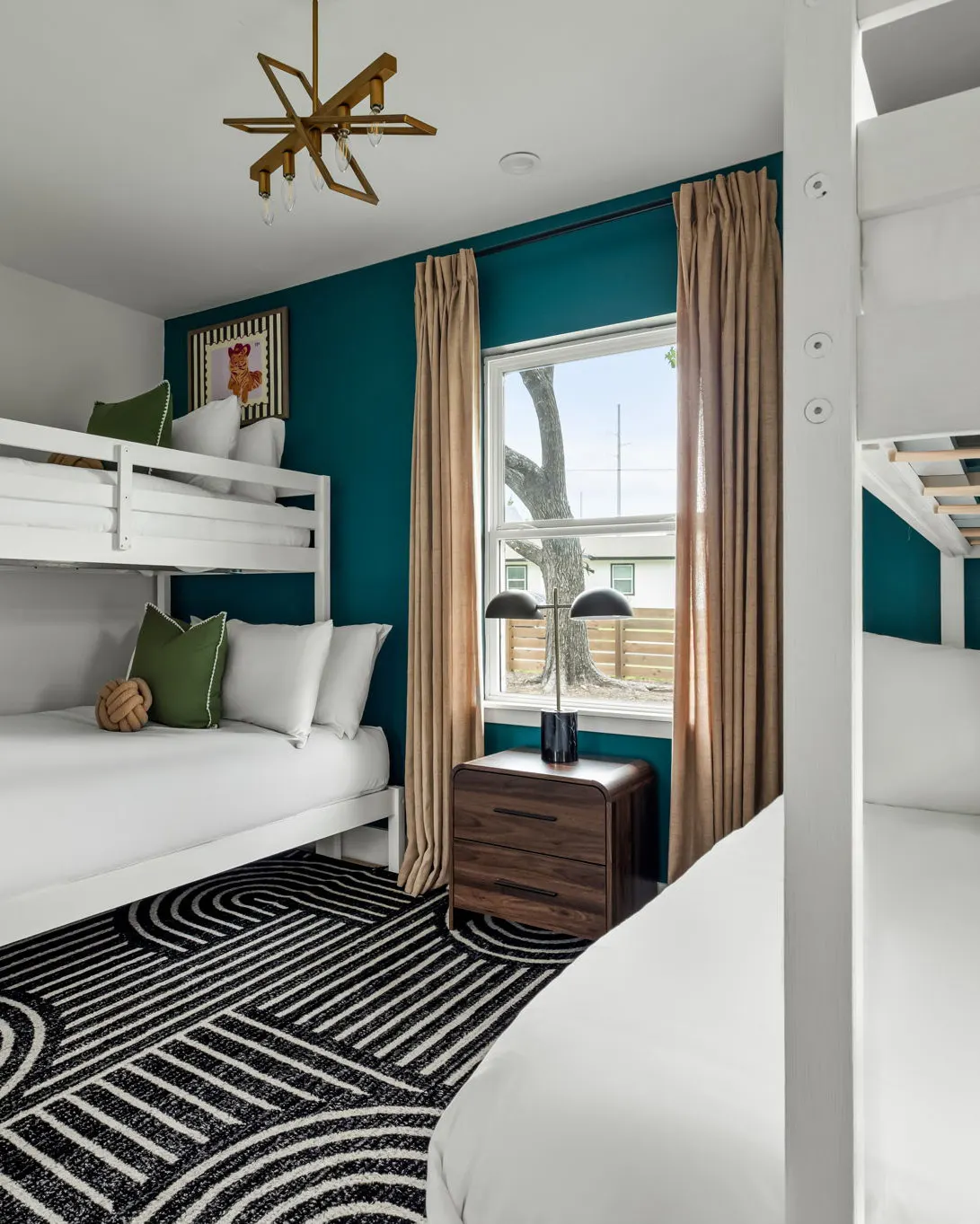 A bunk room with white bunk beds, a teal accent wall and a black and white patterned rug