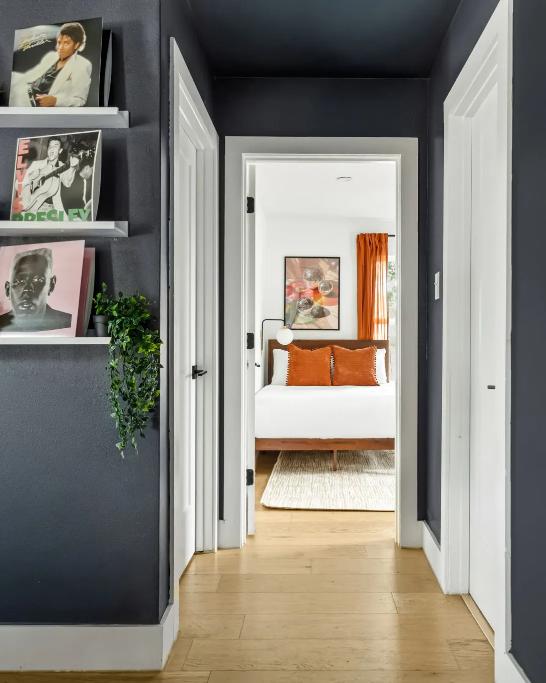 A charcoal hallway lined with album covers on shelves, looking through to a bedroom with rust pillows and a disco ball print