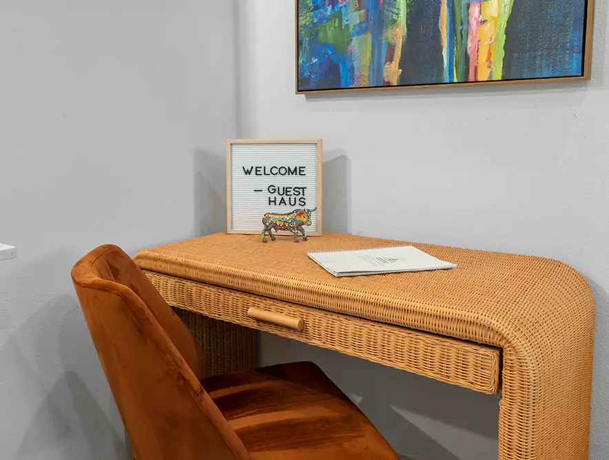 Cozy welcome desk with Guest Haus sign, wicker table, and colorful art