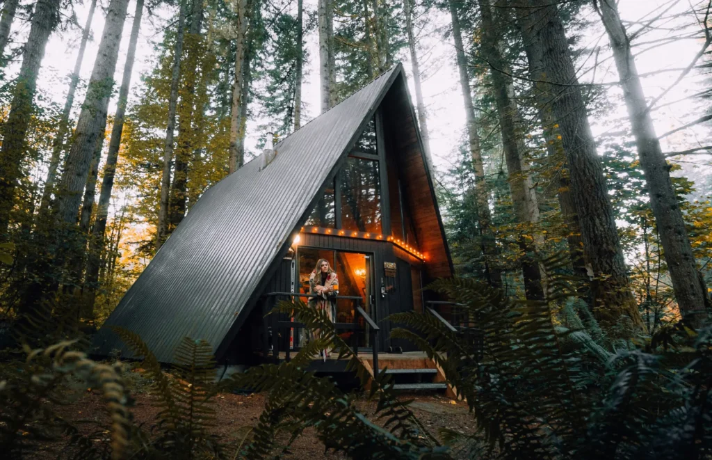 A-frame cabin nestled in a lush forest with warm interior lighting.