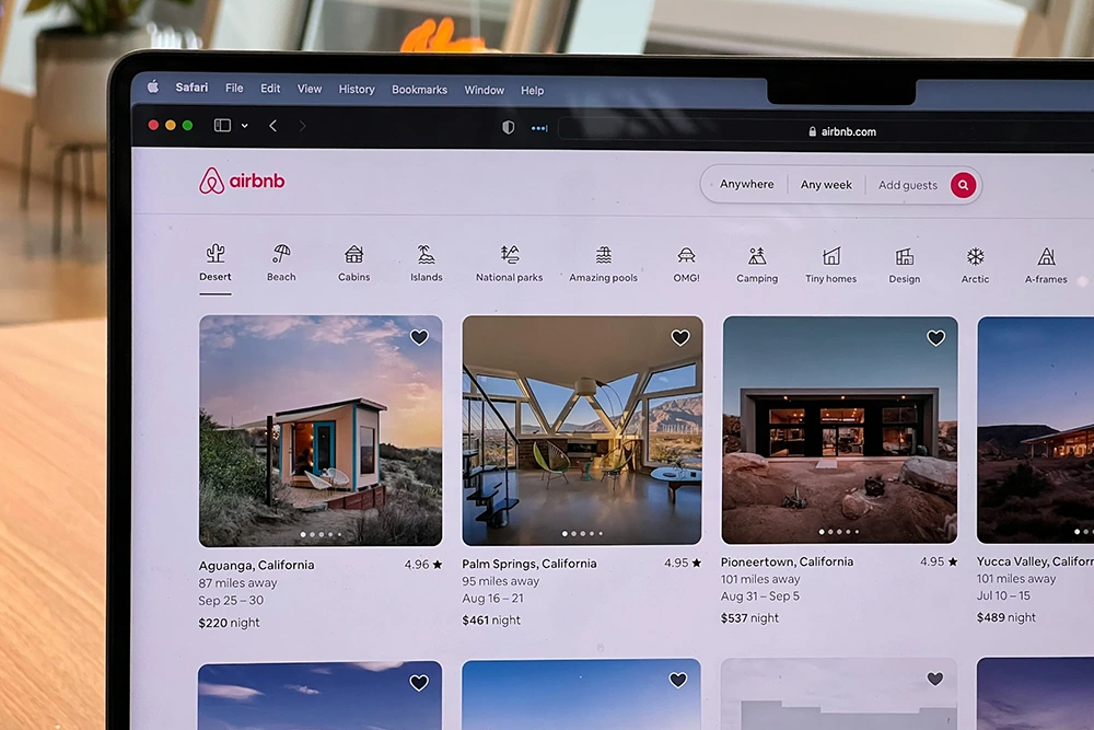 A webpage displays Airbnb listings featuring unique stays in various desert locations in California with categories and booking details visible.