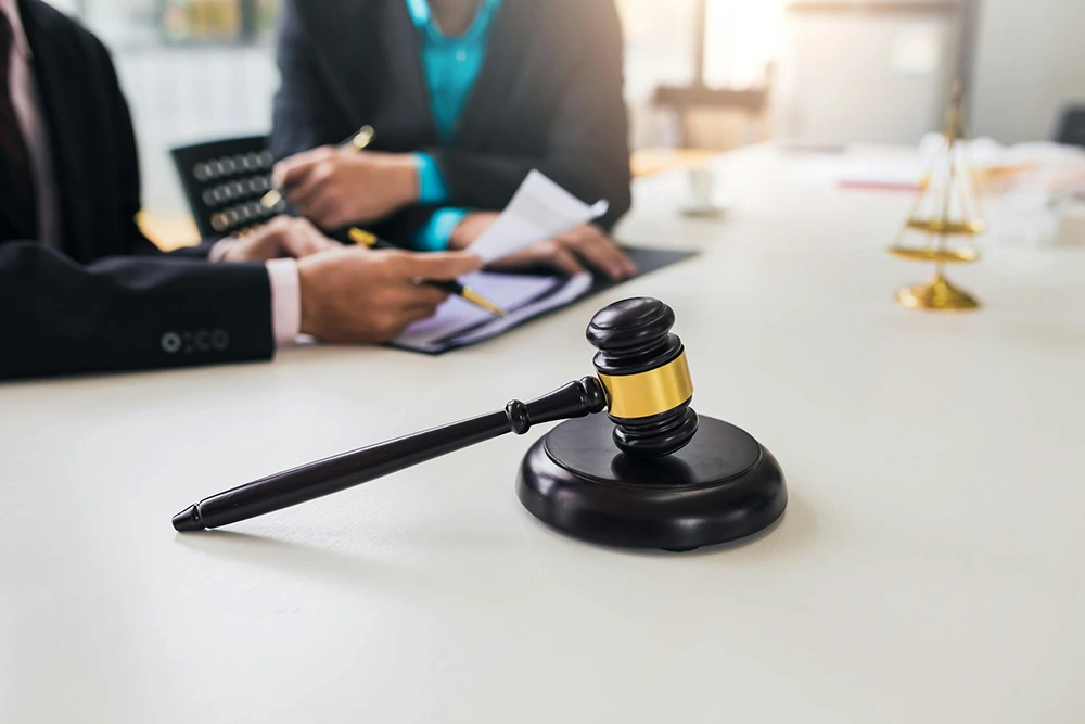 Close-up of a judge's gavel in a courtroom with lawyers consulting in the background.